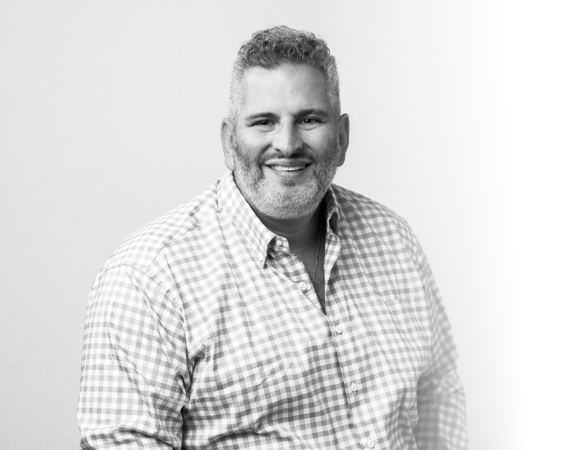 Chris Kourtakis smiling in a checkered shirt, posed against a light background.