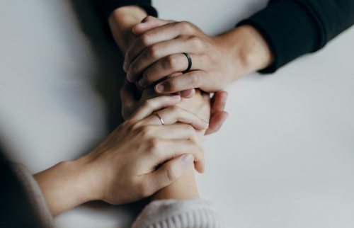 Two pairs of hands holding each other in a supportive gesture on a white surface.