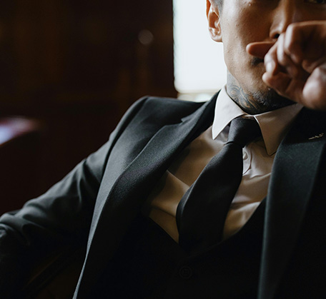 Man in a suit and tie, partially visible, with a thoughtful pose in a dimly lit setting.
