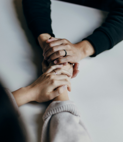 Two pairs of hands holding each other in a supportive gesture on a white surface.