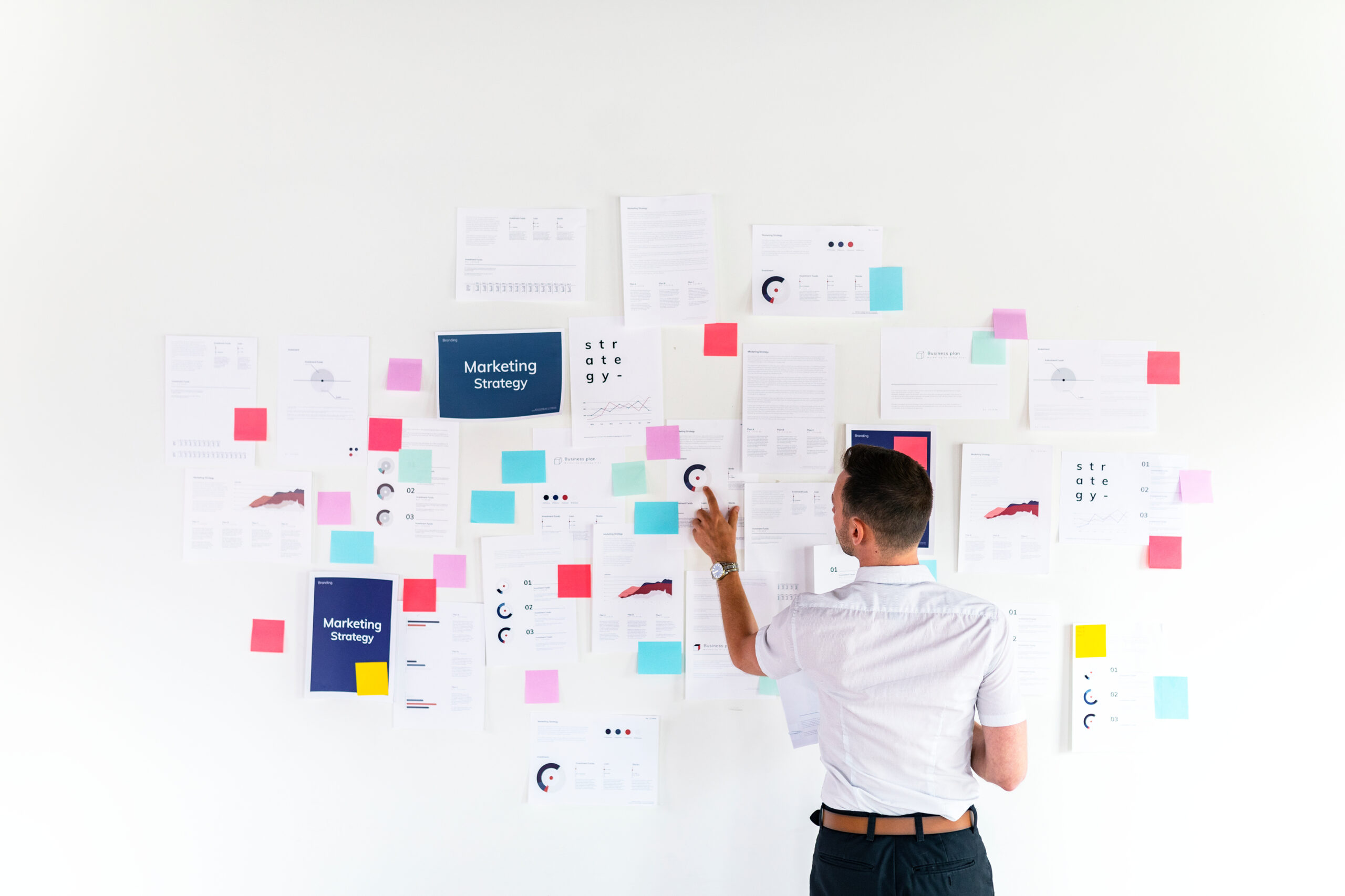 Person organizing strategy documents and sticky notes on a white wall.