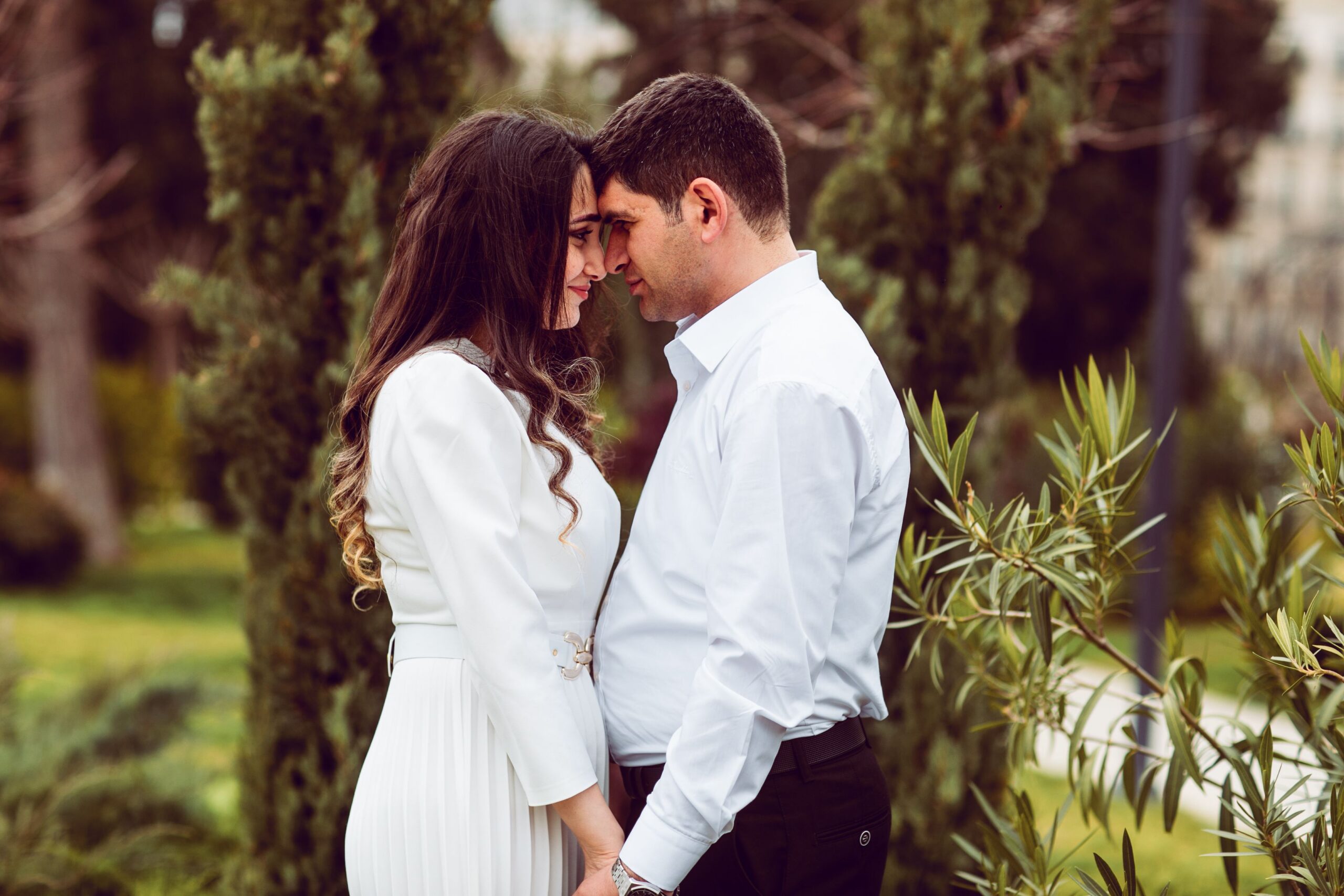 A couple shares a tender moment outdoors, embracing in a lush garden setting.