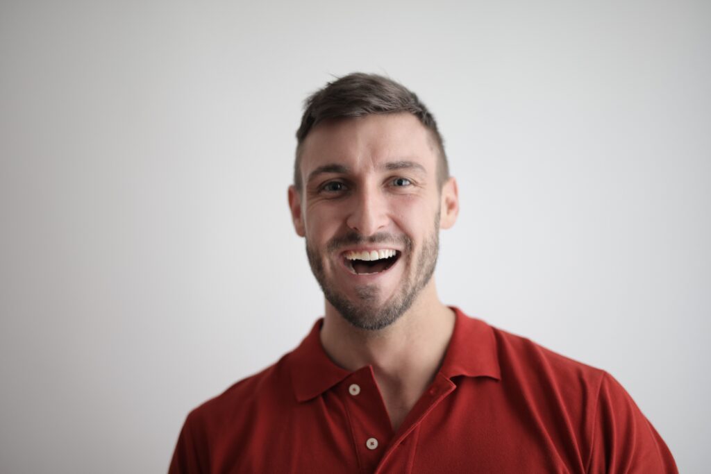 A cheerful man smiling broadly in a red polo shirt against a white background.