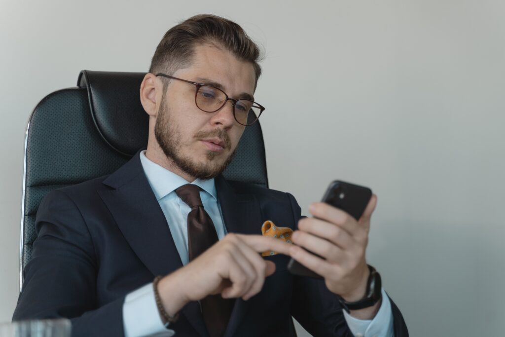 pexels-photo-5439459-5439459 Professional businessman in a formal suit using his smartphone in an office setting.